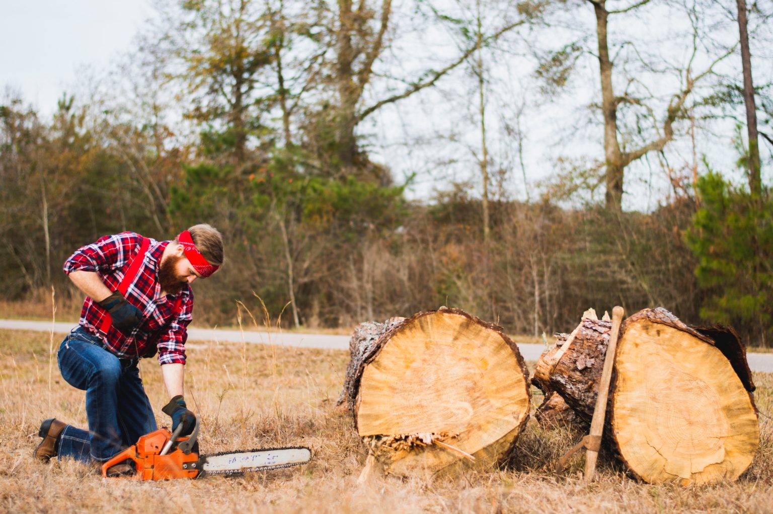 A man in a red plaid shirt kneels to start a chainsaw