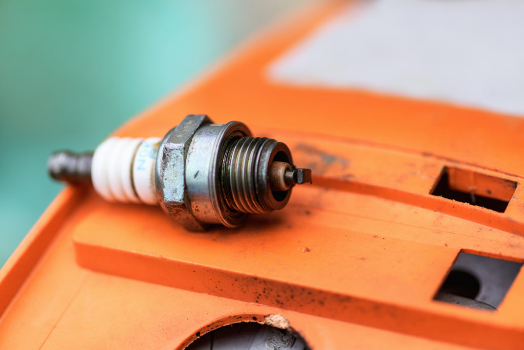 An old, non-working chainsaw spark plug lies on an orange surface