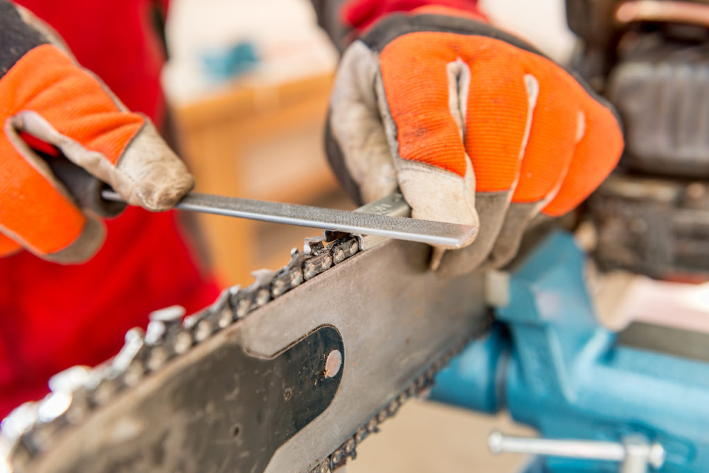 Close up on a man sharpening a chainsaw chain with file.