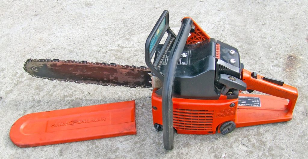 A chainsaw sits on the ground with various components visible.