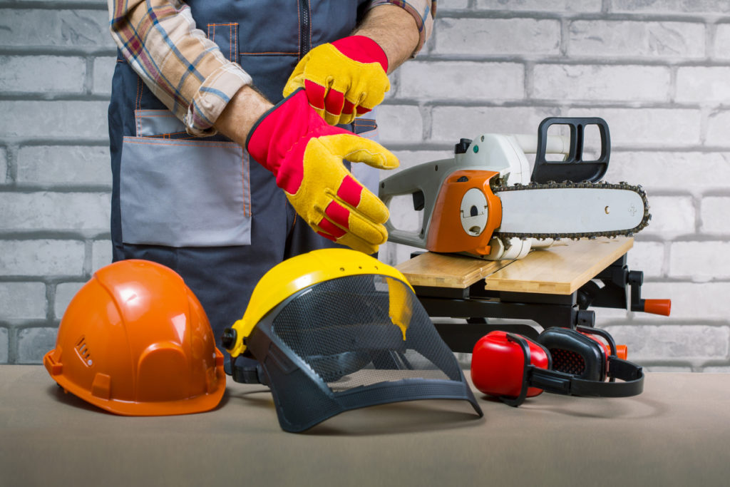 Worker puts protective gloves in workshop. Safety protective equipment arranged on table.