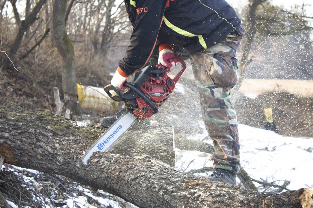 A chainsaw in action cutting wood in wet weather with snow on the ground.